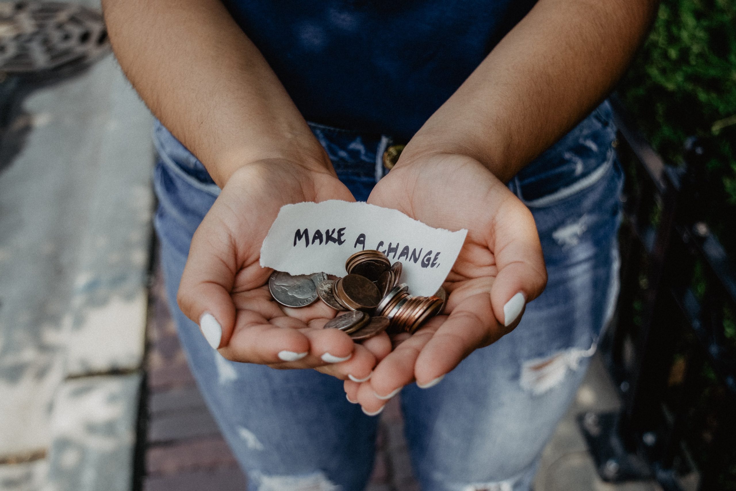 young person holding a handful of coins with a small sign, "make a change"
